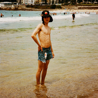 Black UPF 50+ sports hat with neck flap worn at a sunny beach shoreline.