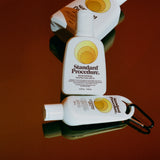 Three Standard Procedure SPF 15 moisturising sunscreen bottles in varying sizes on deep red surface.