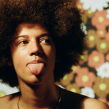 A person with curly hair against a floral background, emphasizing a carefree, sun-kissed look that reflects outdoor surfers sunblock skincare