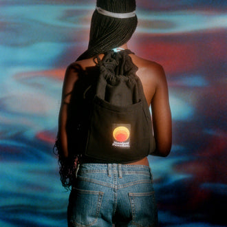 Black Standard Procedure towel bag worn as a drawstring backpack against a sunset-toned backdrop.