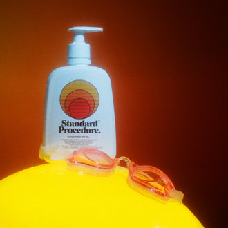 Sunblock lotion SPF 50 bottle placed on a bright yellow surface with swimming goggles against a warm orange background.