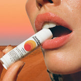 Lip protection SPF 50 balm held near glossy lips with a desert background and warm sunset lighting.