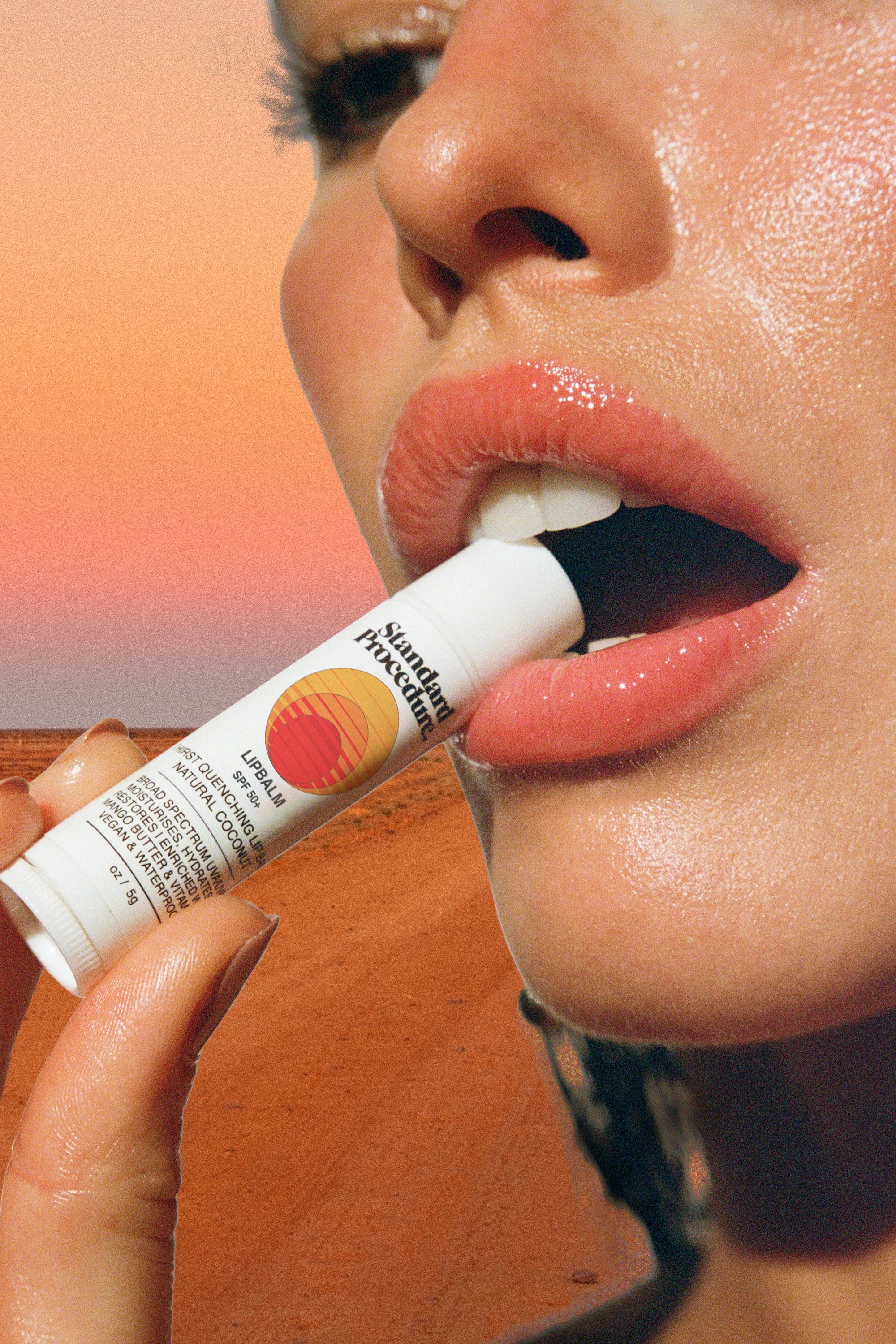 Lip protection SPF 50 balm held near glossy lips with a desert background and warm sunset lighting.