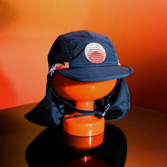 Blue surf hat displayed on an orange stand with a wide brim, neck flap, and adjustable chin strap, featuring the Standard Procedure logo for sun-safe beachwear